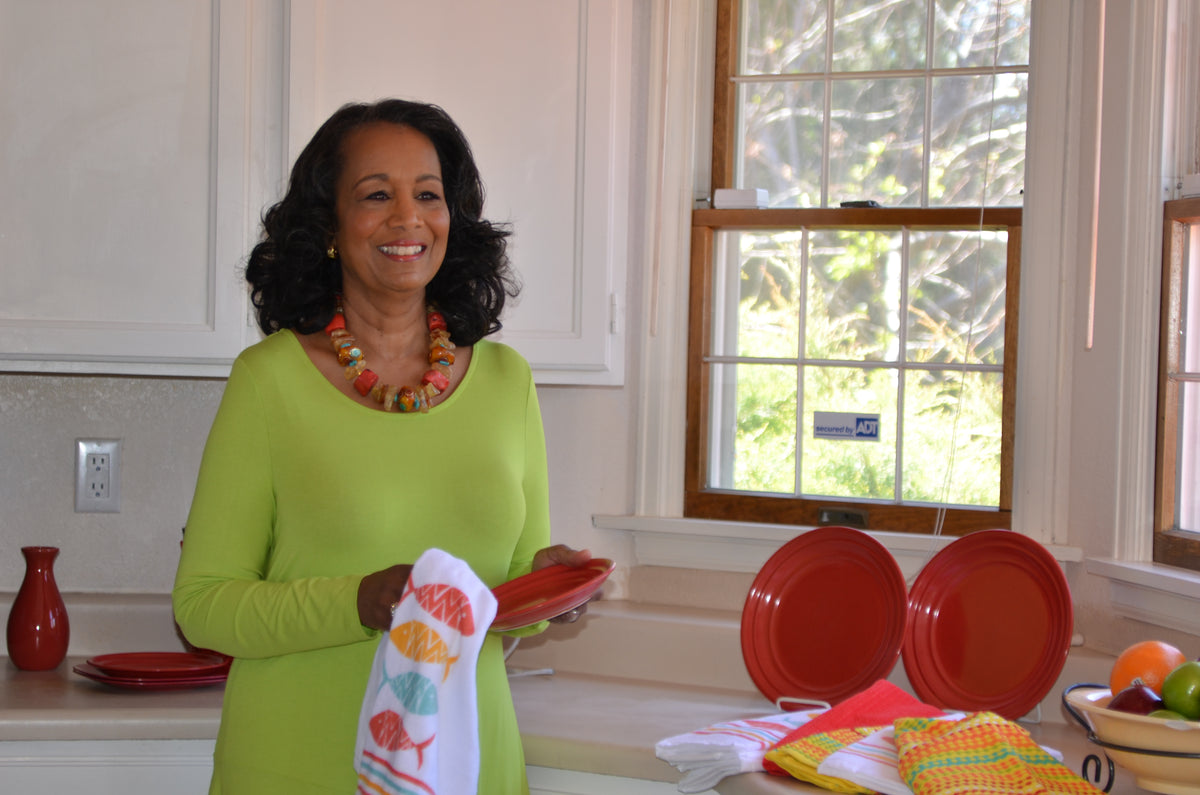 Makeup jewelry and wardrobe styled client in a brightlly lit kitchen wiping a plate with a dish towel