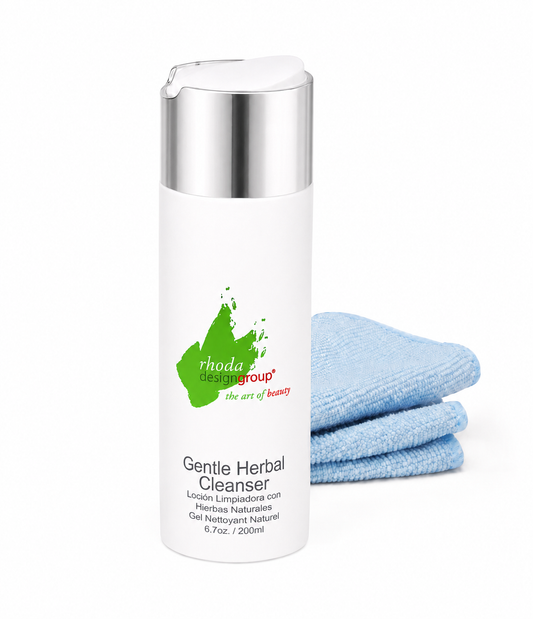 A white bottle of Rhoda Design Group Gentle Herbal Cleanser with a silver cap, shown next to a stack of two light blue microfiber cloths on a white background.