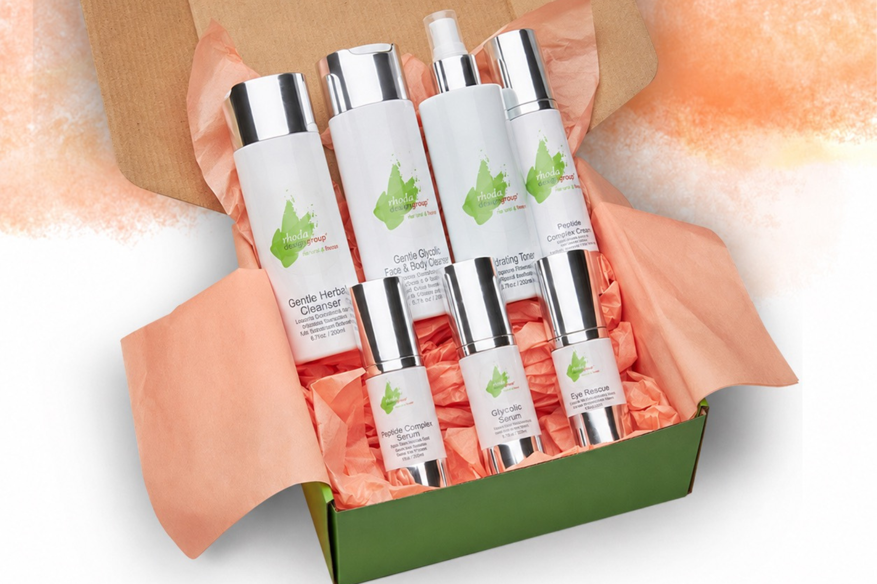 A boxed set of Rhoda Design Group's six white skincare bottles with silver caps and green leaf logos, arranged in a green gift box lined with peach tissue paper on a white background.
